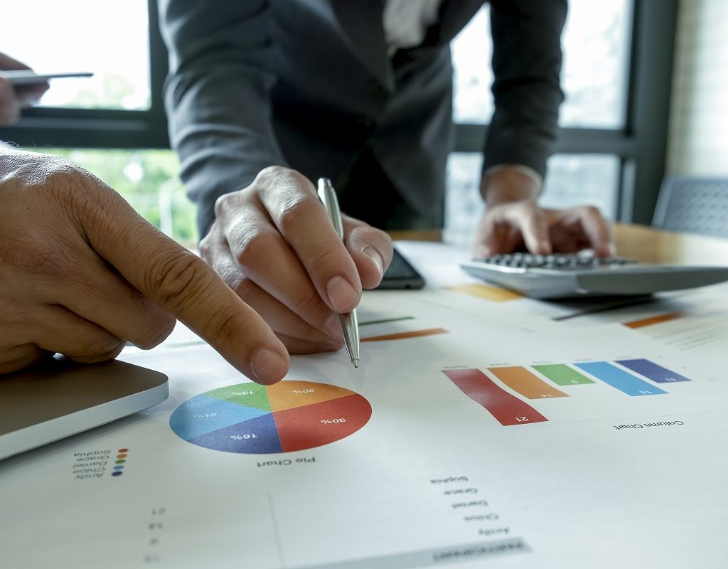 Business team is analyzing graphs on the desk.They point the pen and finger to graphs.