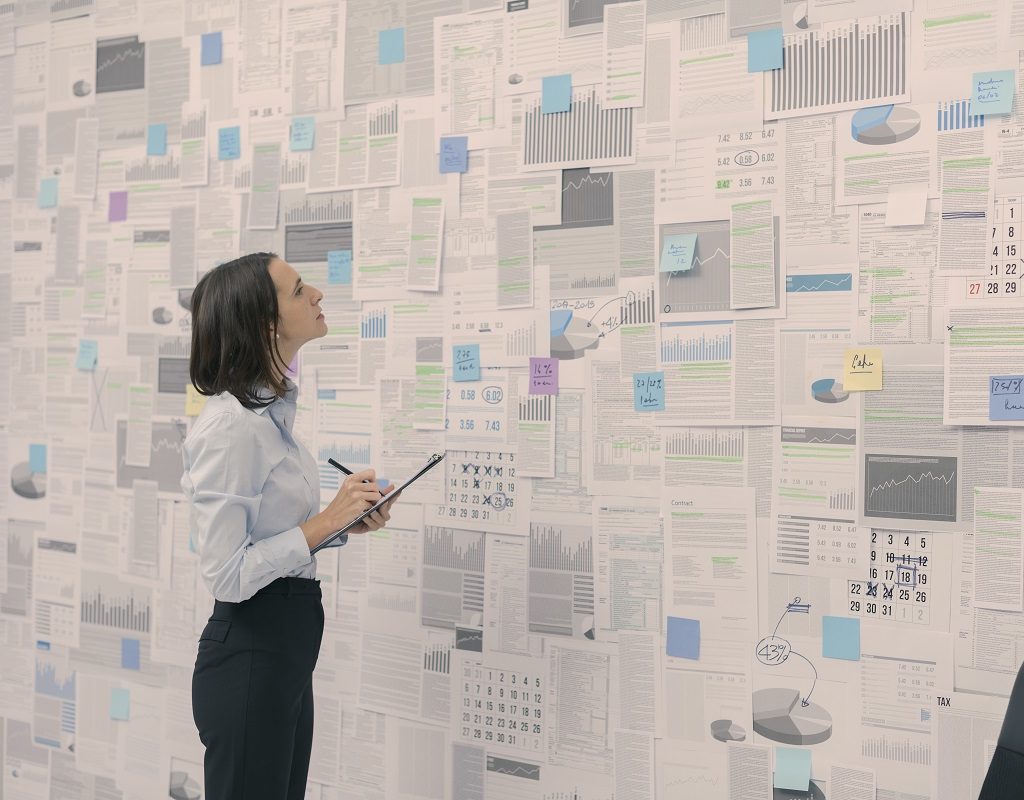 Corporate businesswoman checking financial data and reports hanging on a wall, management and strategy concept