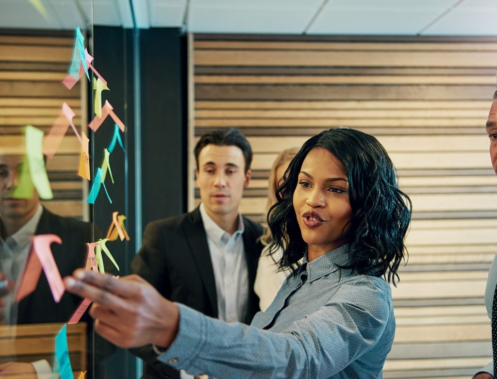 Black business woman in front of mixed business team. Having a standing meeting brainstorming ideas using posters on wall